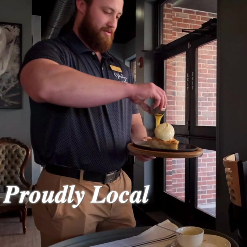 A server pours sauce over a dessert with ice cream on a wooden tray.